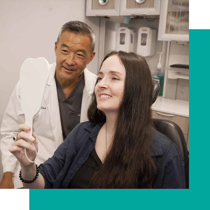 Dr. Chin smiling with a female patient who is looking into a tooth mirror