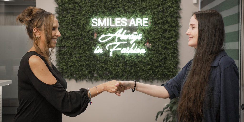 staff member shaking the hand of a female patient in the lobby in front of their sign that says 'smiles are always in fashion"